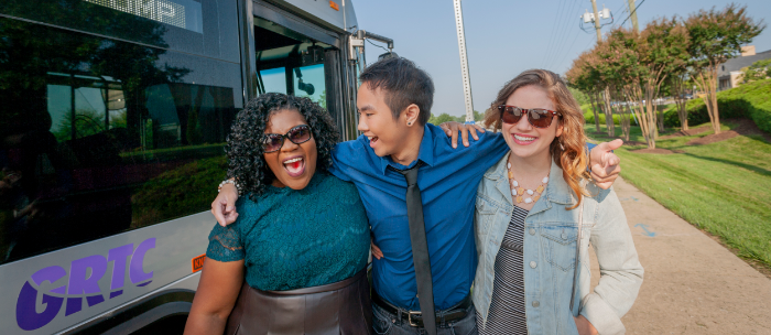 A group of three young people laughing as they walk away from a GRTC bus.