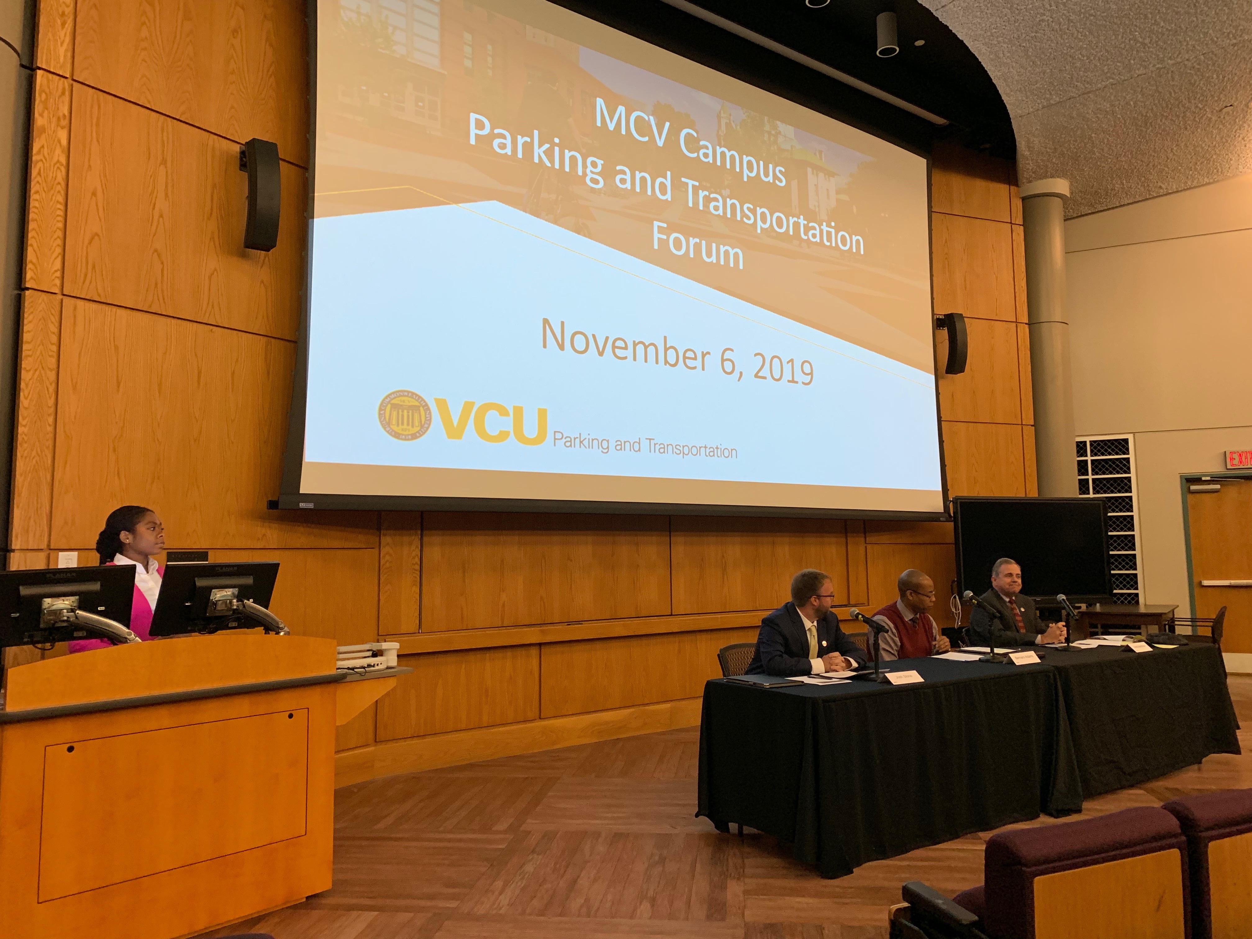 P&T forum in Kontos auditorium with three panel members sitting at table and a woman standing at podium