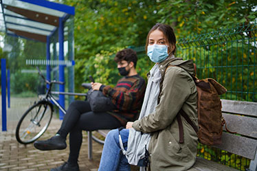 two masked students sitting at bus stop